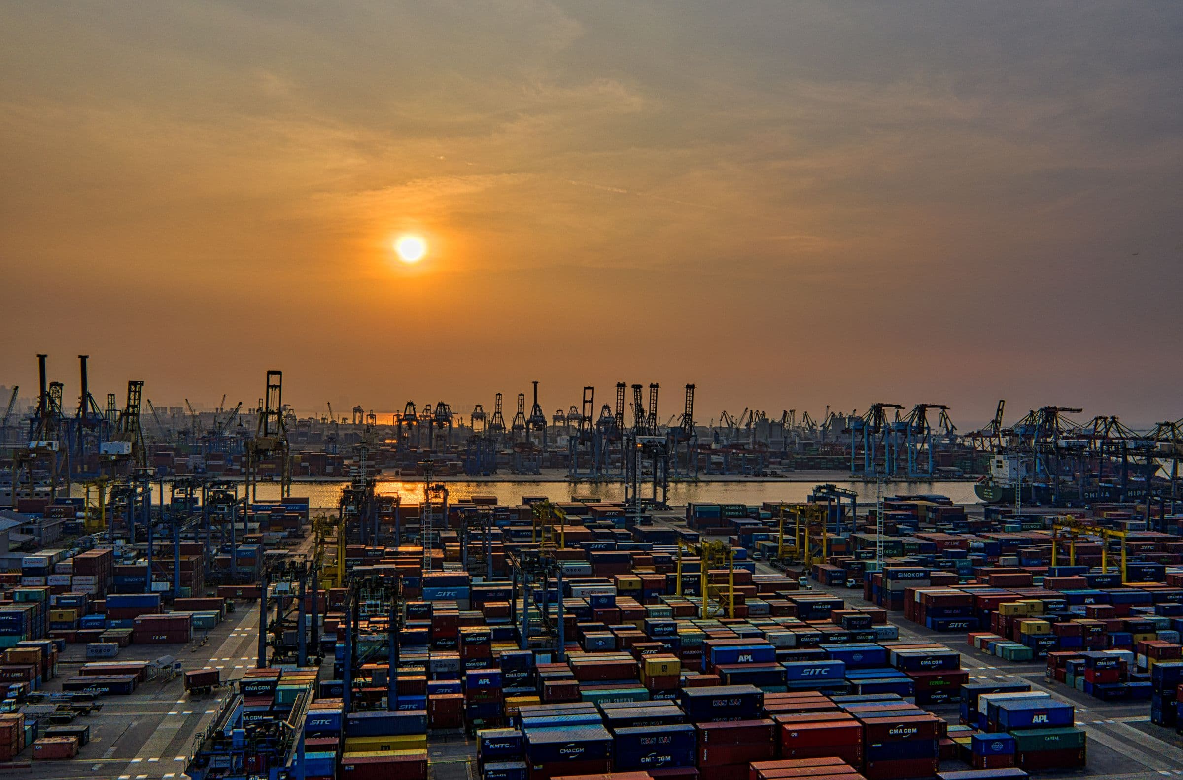 Shipping containers stacked at a busy port at sunset